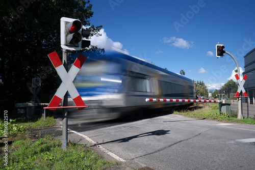 Bahnübergang mit Halbschranke und rotem Signal und vorbeifahrendem Triebwagen - Stockfoto photo