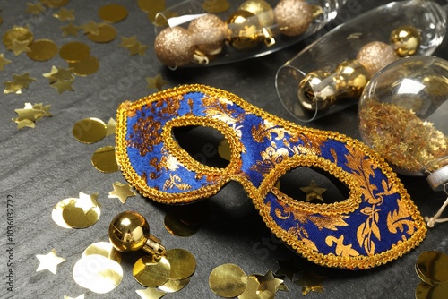 Beautiful golden carnival mask, glasses with decorative balls and confetti on gray textured table, closeup photo