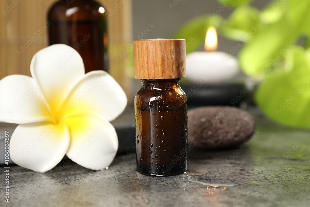 Spa composition with bottles of cosmetic products, plumeria flower and burning candle on grey table, closeup Spa composition with bottles of cosmetic products, plumeria flower and burning candle on grey table, closeup