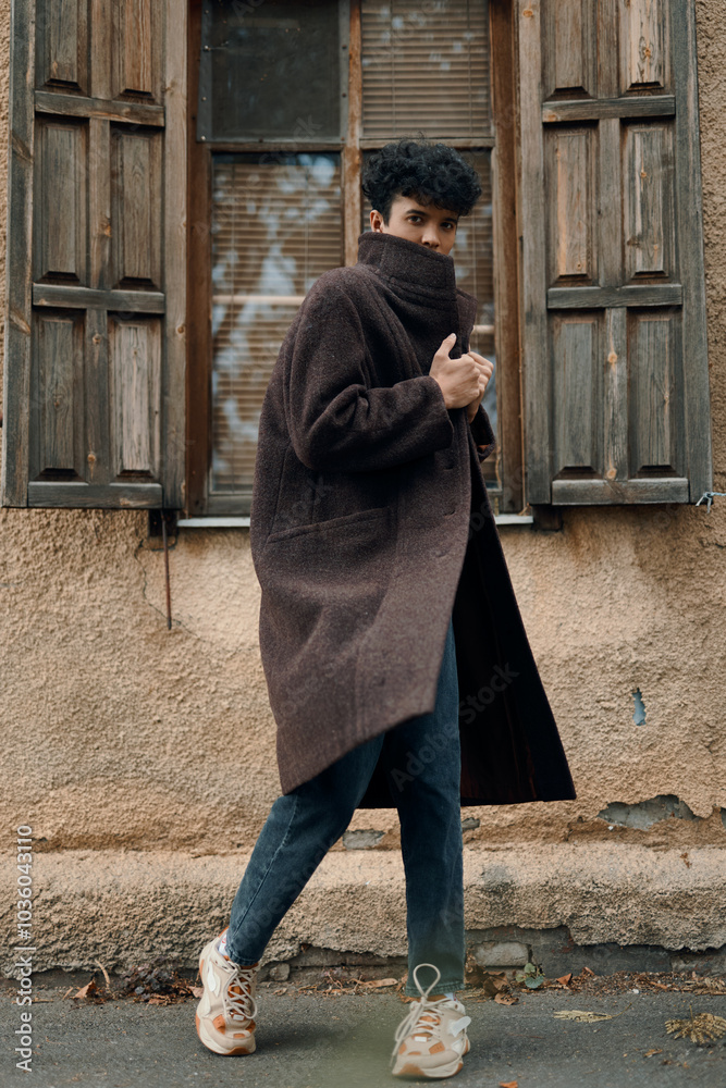 Fashion man in brown coat and jeans walking in front of old building with window in background Fashion man in brown coat and jeans walking in front of old building with window in background