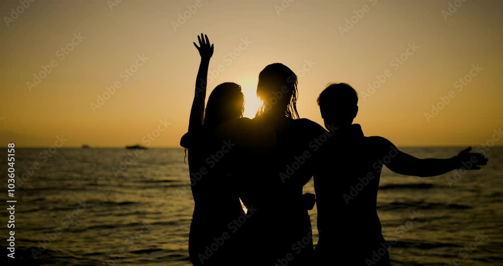 Three friends embracing and waving during a sunset at the beach, evoking a sense of freedom and togetherness