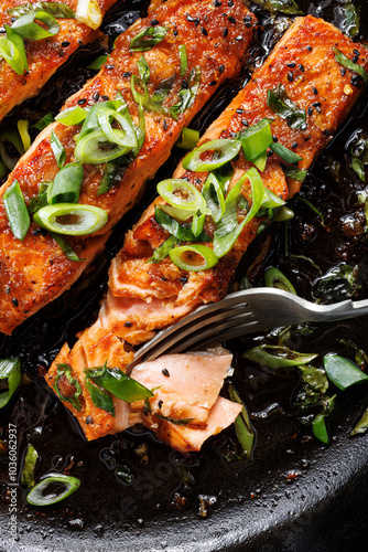 Close-up view of teriyaki salmon sprinkled with chopped scallion in a black baking dish