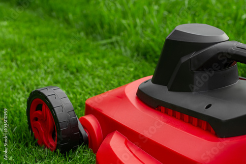 A red and black lawnmower on a green lawn. Mown and unmown grass in the mowing process. photo