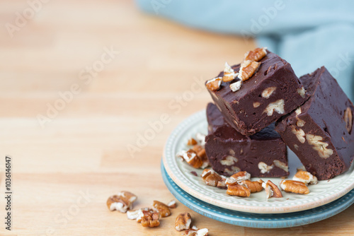 Three Pieces of Homemade Chocolate Pecan Fudge on a Plate with Pecan Pieces Scattered Around on a Kitchen Countertop