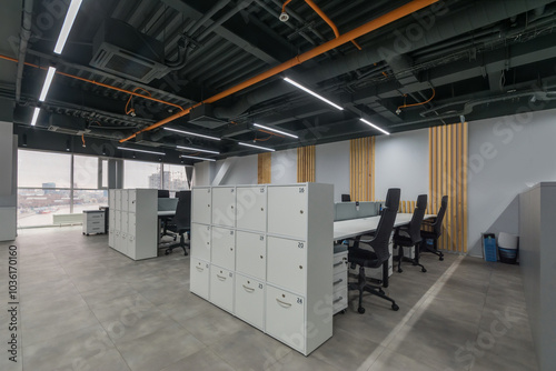 The interior of a modern office with panoramic windows. An open space with cabinets, tables and ergonomic chairs.