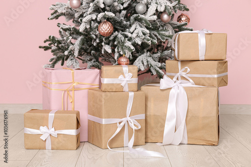 Beautiful decorated Christmas tree with gifts near pink wall