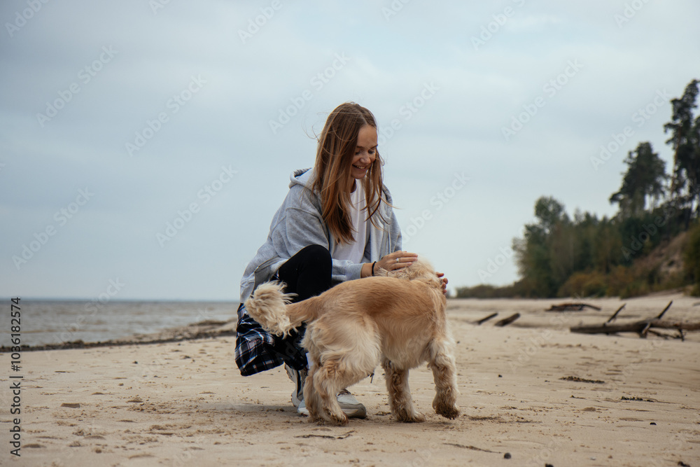 Happy young woman enjoying a walk with her dog along the coast, smiling. Casual autumn style and a peaceful beach backdrop.
