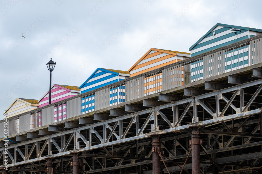 Colorful beach huts line the boardwalk along the seaside, showcasing vibrant stripes against an overcast sky Colorful beach huts line the boardwalk along the seaside, showcasing vibrant stripes against an overcast sky