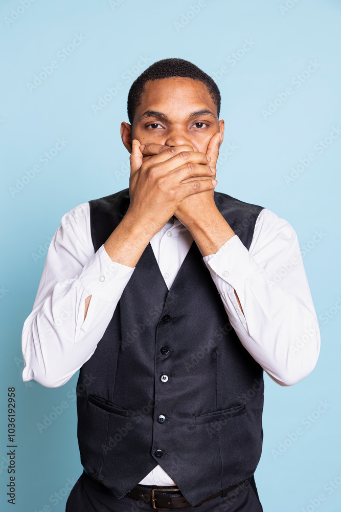 African american doorman showing the three wise monkeys sign against blue background, wearing a suit and tie. Moral wise bellboy covering his mouth for silence, proverbial metaphor. African american doorman showing the three wise monkeys sign against blue background, wearing a suit and tie. Moral wise bellboy covering his mouth for silence, proverbial metaphor.