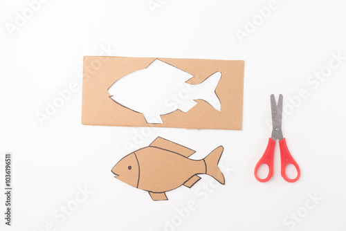 cut out fish shape itself, and a pair of red handled scissors, top view, white background, step in creative process, photo