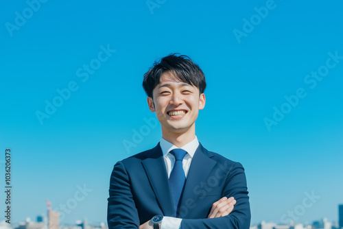 笑顔で腕組みをする若いビジネスマン、アジア人、日本人、空、都市