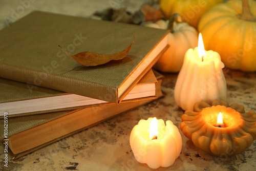 Composition with stack of books, burning candles and autumn leaves on light grunge background, closeup photo