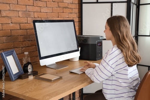 Young woman working with computer and portable power station at table in office