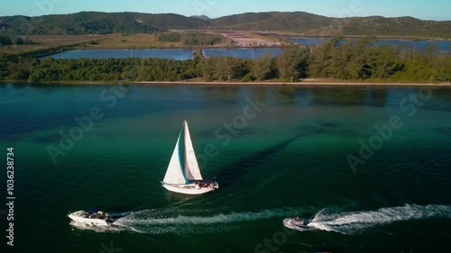 Two boats sailing along the coastline of Itajuru Canal in Cabo Frio, Brazil, with a backdrop of lush greenery. photo