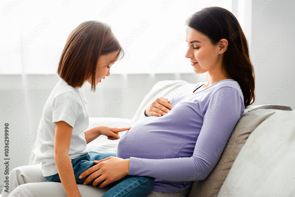 Little girl sitting on pregnant mummy knees and observing big belly, close up, side view Little girl sitting on pregnant mummy knees and observing big belly, close up, side view