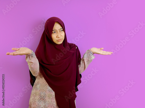 Questioning concept or don't know expression of South east Asian Indonesian Female with Hijab olive color or Gamis on purple background.  photo