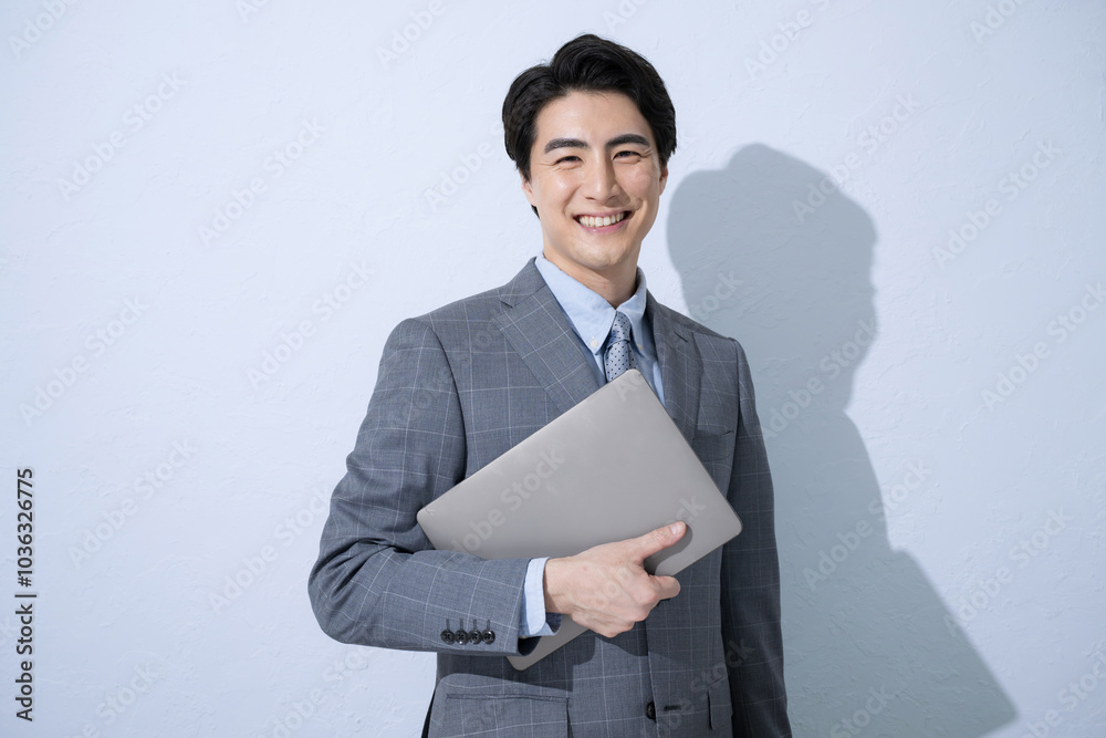 Young handsome businessman holding (holding) computer, looking at camera and smiling, light blue background Young handsome businessman holding (holding) computer, looking at camera and smiling, light blue background
