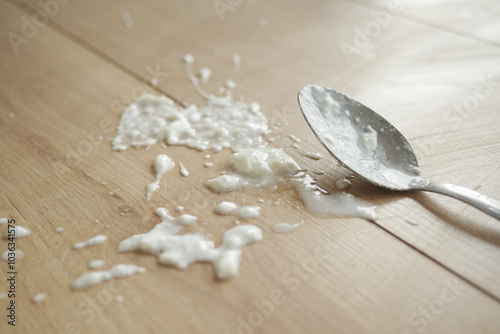 There was an accident involving spilled yogurt on a wooden floor, with a spoon in focus