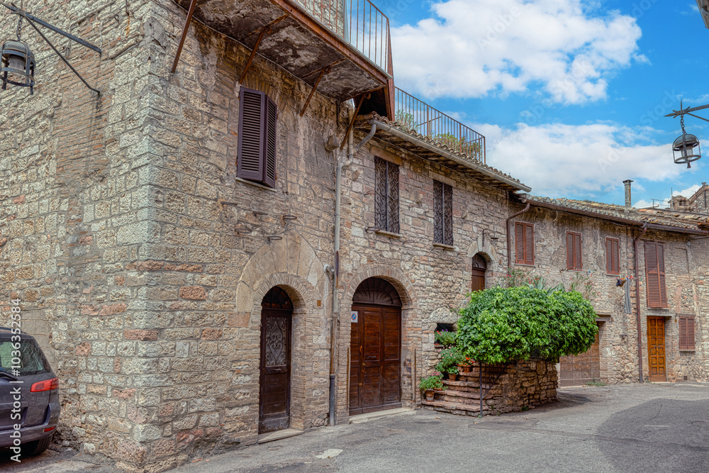 A charming cobblestone street in medieval Assisi, (Umbria, Italy), featuring ancient stone buildings and vibrant flower pots
