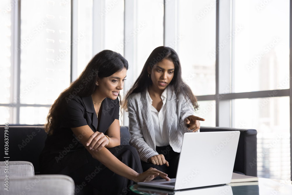 Two busy diverse female colleagues talking at laptop, pointing a screen, discussing work project, teamwork strategy, watching online product , website, presentation on internet Two busy diverse female colleagues talking at laptop, pointing a screen, discussing work project, teamwork strategy, watching online product , website, presentation on internet