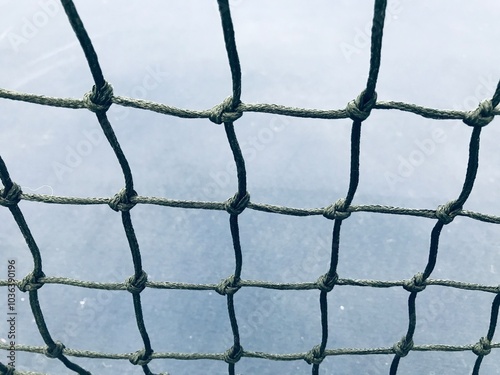 close up shot of a black plastic net stretched into a grid with a blurred blue tennis court on background
