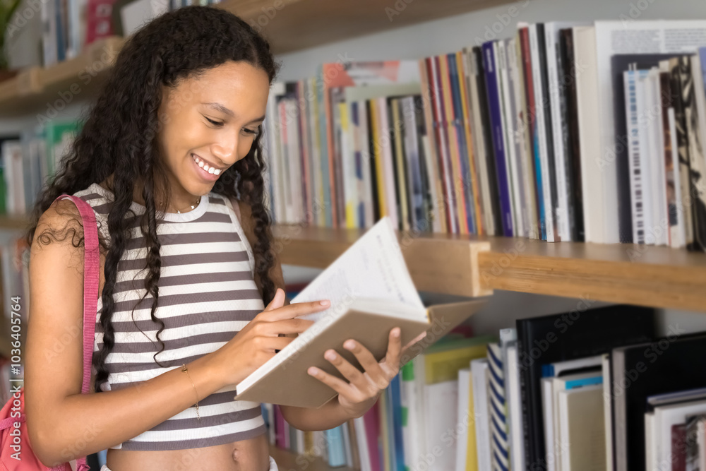 Positive young African American student girl reading book in university library, standing at bookshelves, enjoying learning process, choosing textbook for education Positive young African American student girl reading book in university library, standing at bookshelves, enjoying learning process, choosing textbook for education