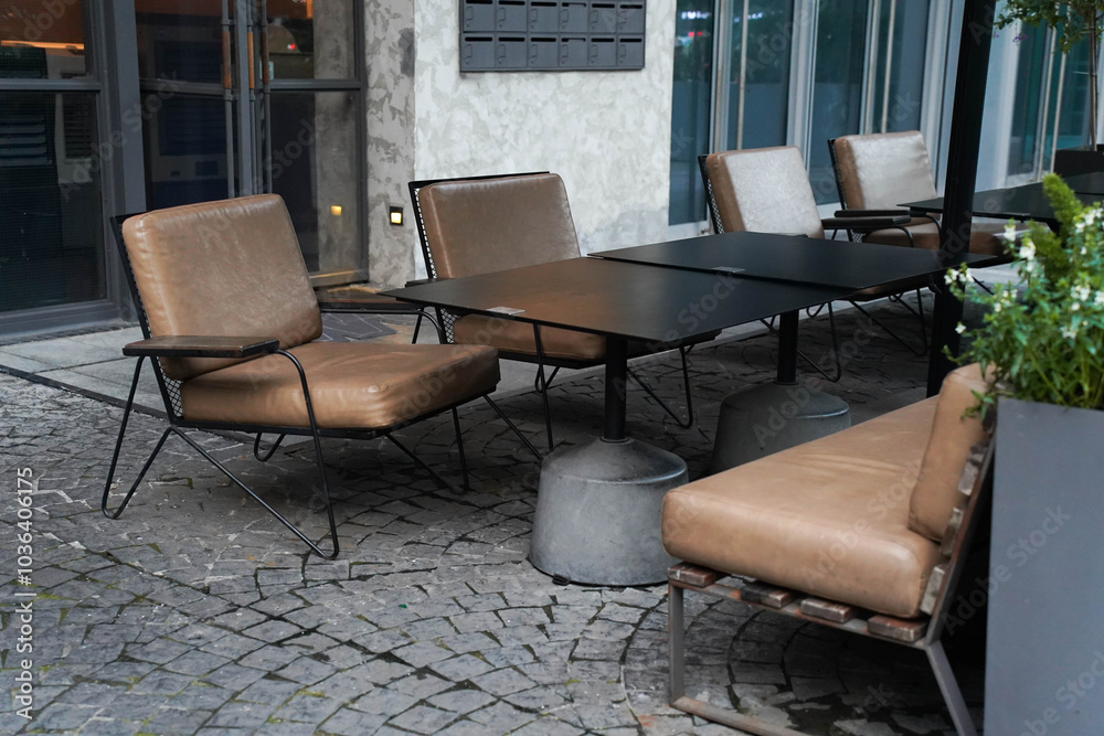 Outdoor café setting with empty tables and chairs, surrounded by plants.