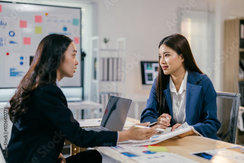 Two young businesswomen are having a serious conversation in a meeting, analyzing charts and data on a desk with a laptop