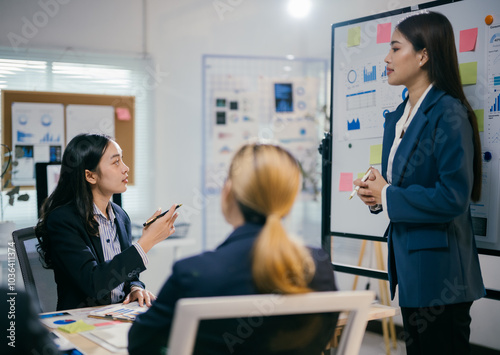 Businesswomen are having a productive meeting, discussing ideas and strategies while looking at a whiteboard with charts and graphs