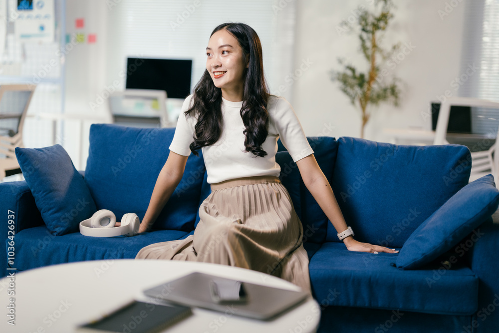 Young asian businesswoman sitting on a blue sofa in a modern office, enjoying a moment of relaxation after a productive day Young asian businesswoman sitting on a blue sofa in a modern office, enjoying a moment of relaxation after a productive day