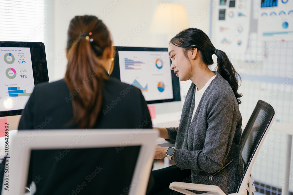 © Parichat - Two asian businesswomen are working together in the office. They are looking at charts and graphs on a computer screen, analyzing financial data