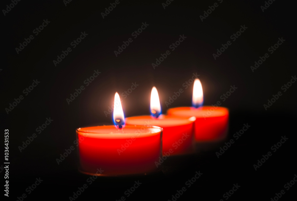 Close-up of three burning candles on black background with copy space on top. Close-up of three burning candles on black background with copy space on top.