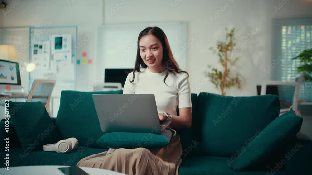 Young woman smiles while opening and closing her laptop on a green sofa in her home office. The scene captures a relaxed atmosphere, blending work and comfort seamlessly Young woman smiles while opening and closing her laptop on a green sofa in her home office. The scene captures a relaxed atmosphere, blending work and comfort seamlessly