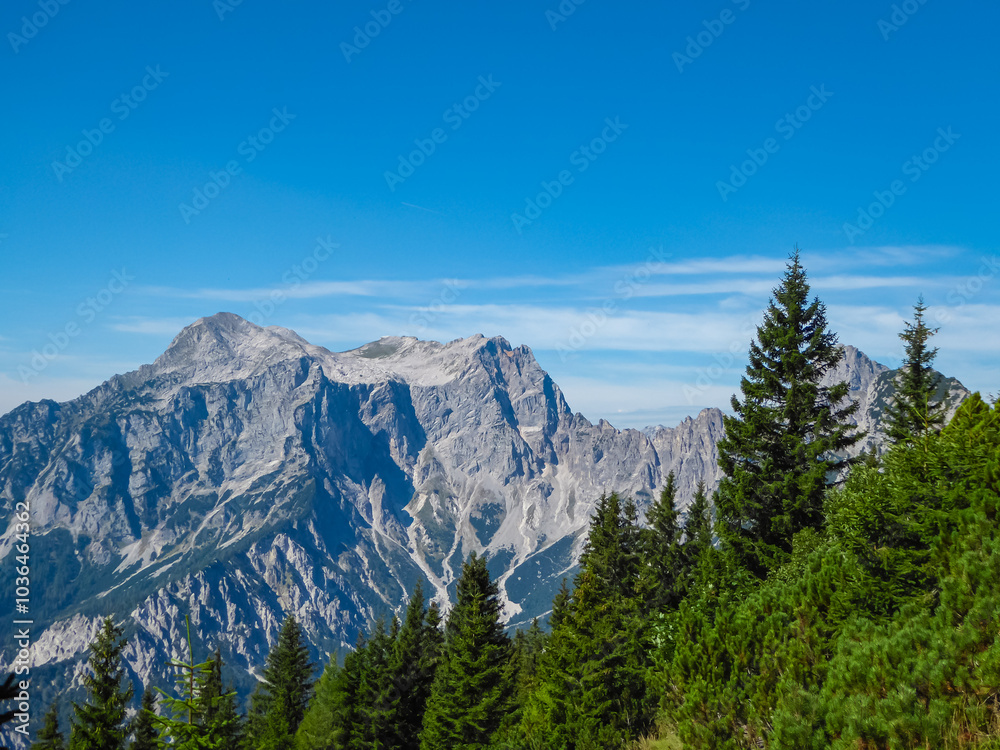 Panoramic view of majestic mountain range of Gesäuse, Ennstal Alps, Styria, Austria. Towering, jagged peaks rise up in Austrian Alps. Dense alpine forests cover the hillsides. Wanderlust in summer