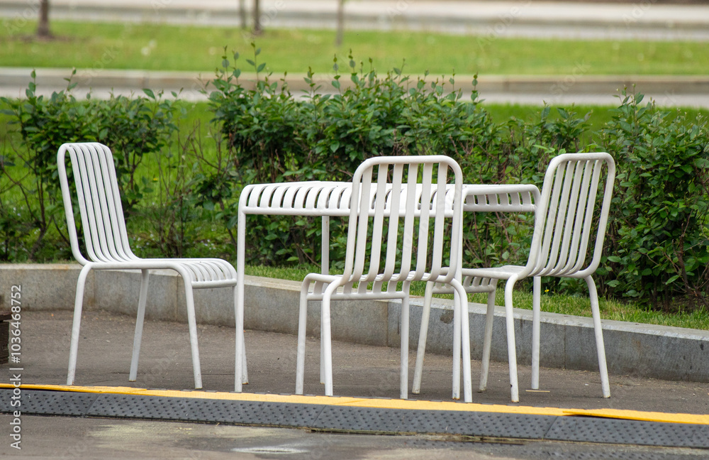 A white metal table with four chairs is sitting on a sidewalk A white metal table with four chairs is sitting on a sidewalk