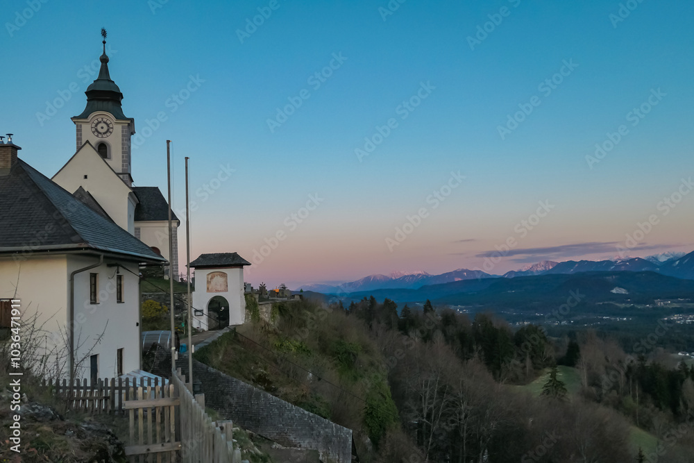 Golden sunset light on Sternberg church on hilltop looking at mountain peaks of Karawanks and Julian Alps. Tranquil alpine landscape of idyllic Rosental valley seen from Wernberg, Carinthia, Austria Golden sunset light on Sternberg church on hilltop looking at mountain peaks of Karawanks and Julian Alps. Tranquil alpine landscape of idyllic Rosental valley seen from Wernberg, Carinthia, Austria