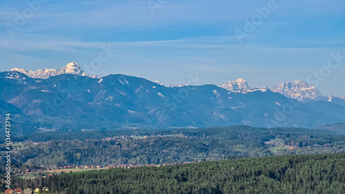 Scenic view of snow-capped mountain peak Jof Montasio in Julian Alps seen from Sternberg in Wernberg, Carinthia, Austria. Valley covered by idyllic forest in Austrian Alps. Tranquil alpine landscape photo