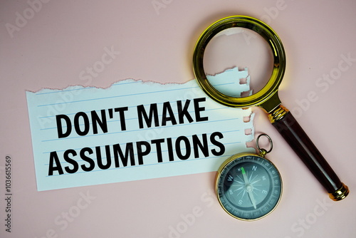 Don't make assumptions text written on paper torn with compass and magnifying glass top view on pink background photo