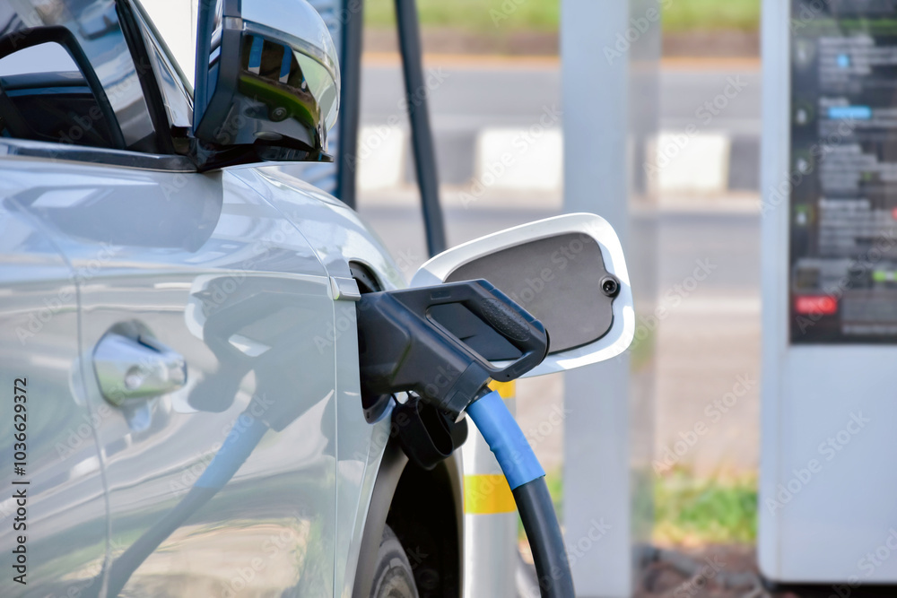 A white electric car is charging its battery system at a service station at the afternoon of the day. A white electric car is charging its battery system at a service station at the afternoon of the day.