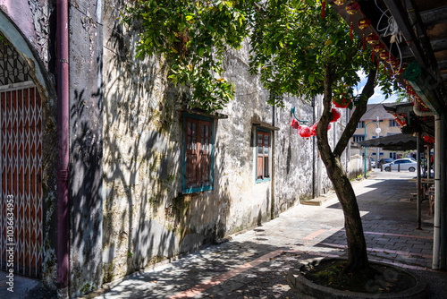 Pedestrian Alley walkway with dappled light and shadows from trees on summer day, with Chinese Lanterns and decorations hanging overhead, in Kuching, Sarawak, Malaysia.