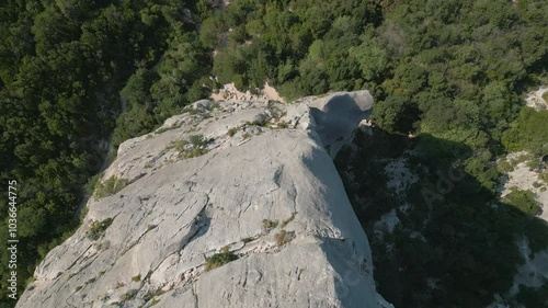 Tilt-down aerial drone footage from the top of the spectacular Punta Caroddi limestone spire down to the forest at Cala Goloritze on the Gulf of Orosei on the island of Sardinia in Italy photo