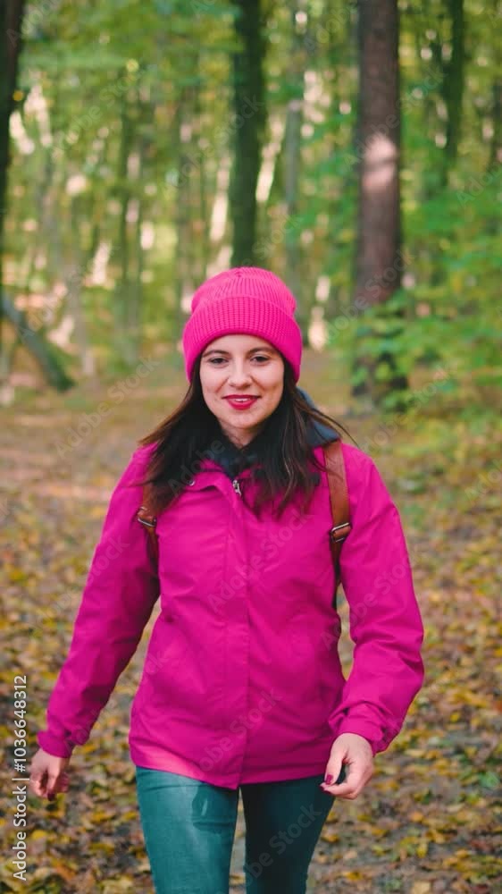 Attractive, positive young woman in a pink jacket, jeans and backpack walking through an autumn forest, slow motion Attractive, positive young woman in a pink jacket, jeans and backpack walking through an autumn forest, slow motion
