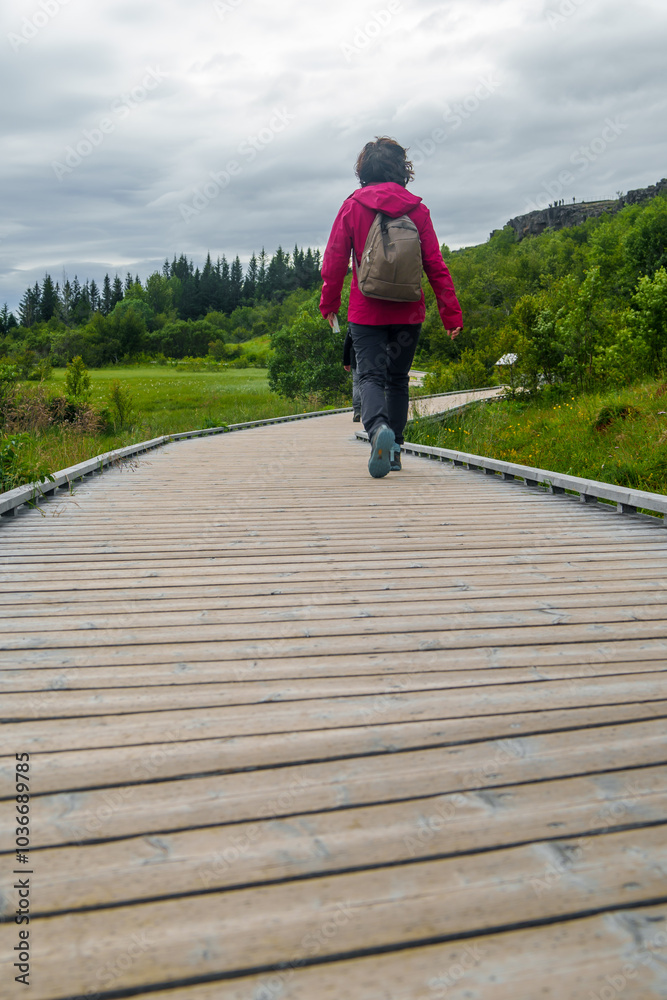 Obraz premium Woman walking on a wooden path in pingvellir National Park, Iceland