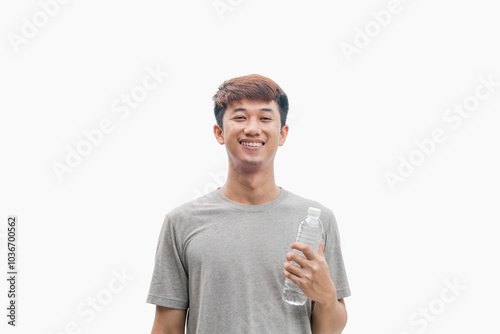 A handsome Asian man in a grey t-shirt holding a water bottle with a happy and confident smiling face on a grey background. Healthy drinking water concept. Suggesting the benefits of water