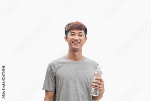 A handsome Asian man in a grey t-shirt holding a water bottle with a happy and confident smiling face on a grey background. Healthy drinking water concept. Suggesting the benefits of water