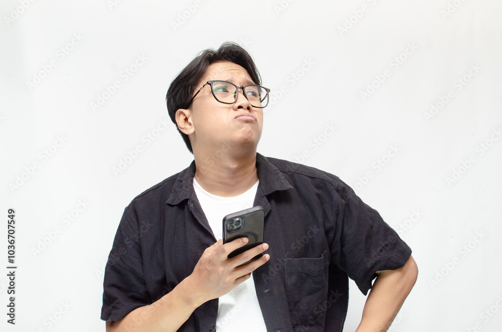 a sad and overthinking young Asian man in a pensive mood holding a phone with a sad and thoughtful expression. Asian man holding phone while questioning, wondering and crying. a sad and overthinking young Asian man in a pensive mood holding a phone with a sad and thoughtful expression. Asian man holding phone while questioning, wondering and crying.