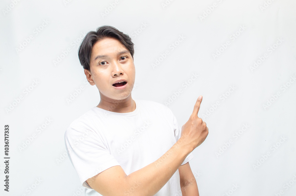 Atrractive young asian man in white t-shirt pointing his finger to advertise something. handsome asian man promoting something and pointing his finger to copy space showing discount or promotion. Atrractive young asian man in white t-shirt pointing his finger to advertise something. handsome asian man promoting something and pointing his finger to copy space showing discount or promotion.