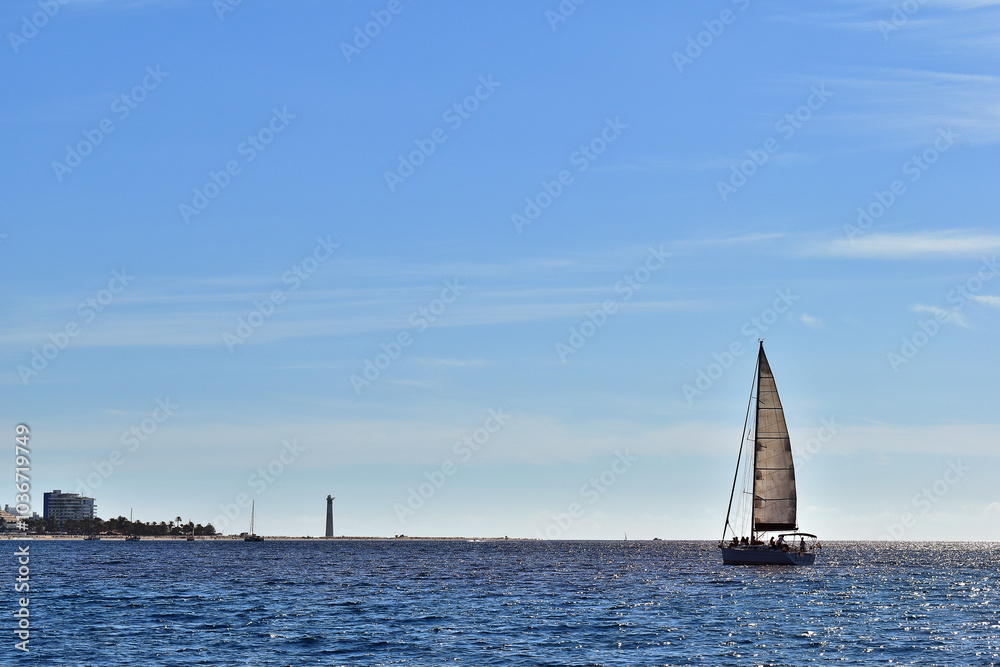 Segelboot vor der Küste von Morro Jable mit Leuchtturm Segelboot vor der Küste von Morro Jable mit Leuchtturm