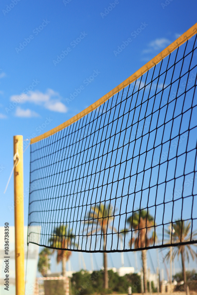 Volleyball net fragment on the beach against blue sky and palm trees. Beach volleyball net close-up. Sports, beach volleyball. Active recreation concept. Yellow net detail. Sports ground Volleyball net fragment on the beach against blue sky and palm trees. Beach volleyball net close-up. Sports, beach volleyball. Active recreation concept. Yellow net detail. Sports ground