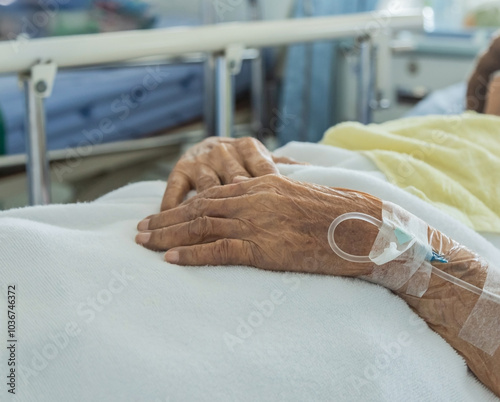Close up intravenous saline for injection plug in hand of elderly patient lying in the hospital bed room